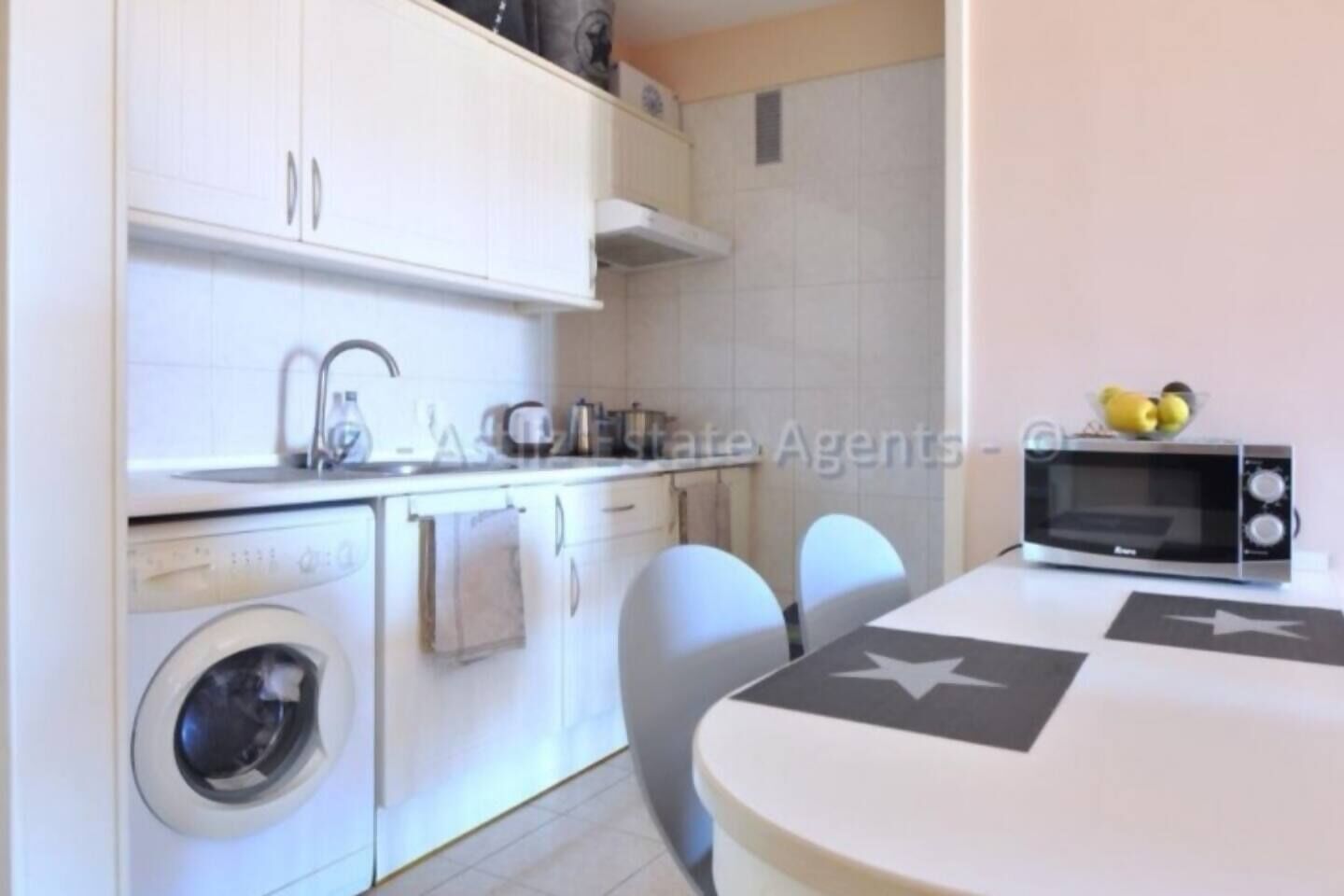 A compact kitchen with a washing machine, a microwave, and a dining table with chairs.
