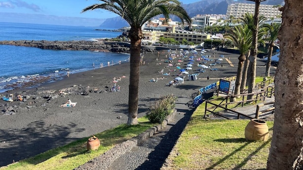 Una playa con sombrillas, palmeras y una costa rocosa.