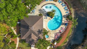 Vista aérea de un resort con una amplia piscina circular, tumbonas y un edificio de techo inclinado.