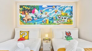 Una habitación de hotel con dos camas, cada una con un cojín que presenta un personaje de un videojuego. Encima de las camas hay un cuadro de una escena de videojuego.