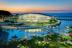 A modern building with a glass facade, surrounded by a waterfront promenade with umbrellas and palm trees. - Zen Crescent Sanctuary Cozy - Modern - Unique (Darwin)