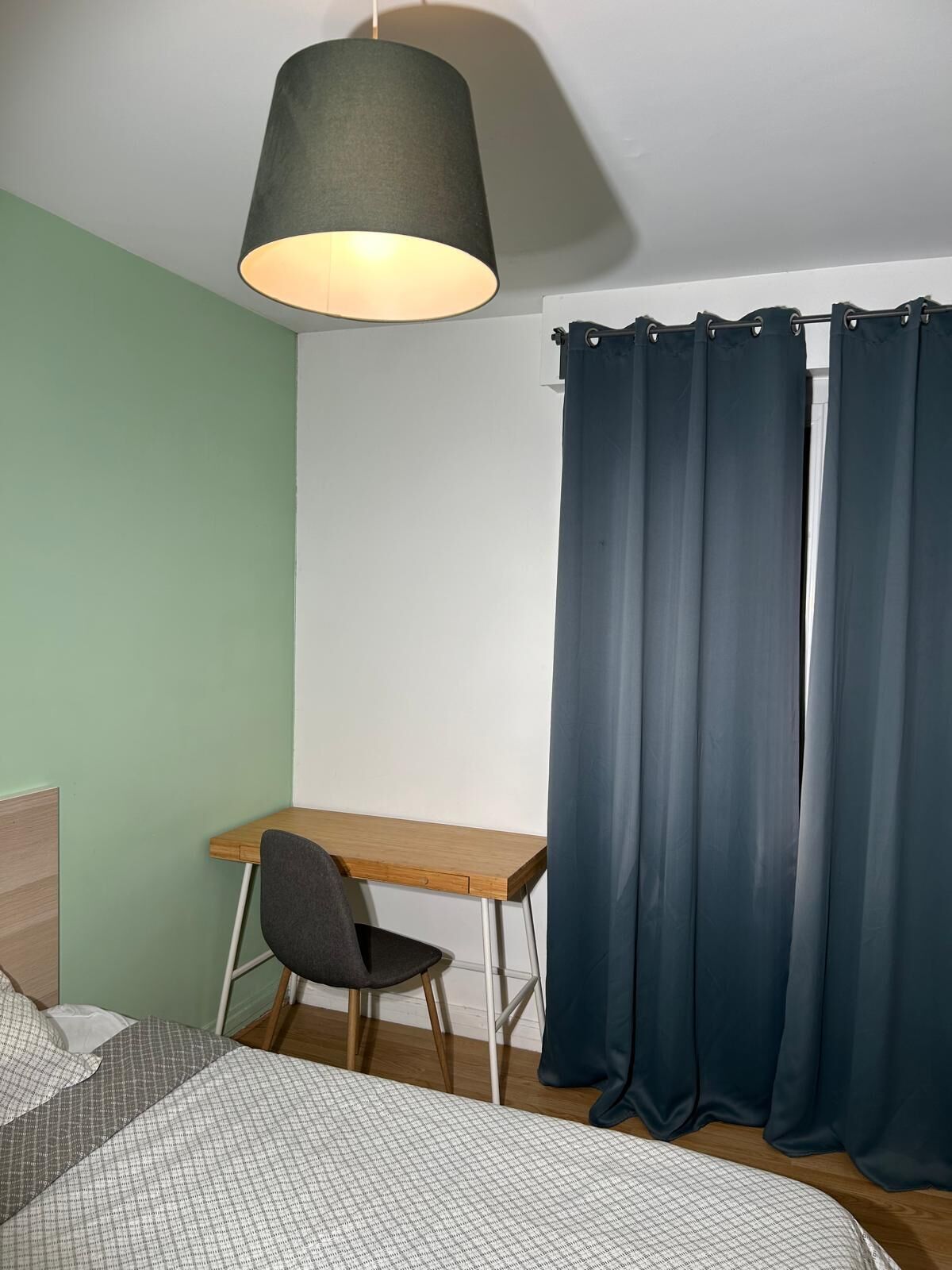 A room with a bed, a desk, a chair, and a curtain.