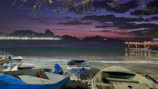 Une plage avec des bateaux et la silhouette d’une ville au crépuscule.