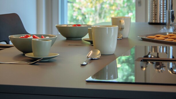 Una mesa de comedor con cuencos, tazas y cucharas, frente a una ventana con vistas a follaje.