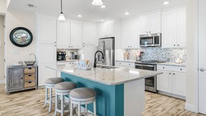 Une cuisine moderne avec des meubles blancs, un îlot central doté de tabourets, des appareils en acier inoxydable et un pare-feu orné de motifs en mosaïque.