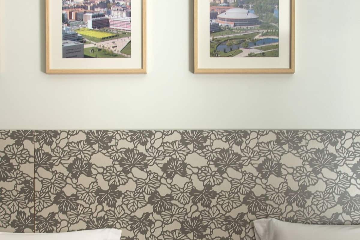 Une chambre d’hôtel avec deux lits, une tête de lit à motifs floraux, une petite commode blanche avec des tiroirs et deux tableaux encadrés représentant des paysages urbains accrochés au mur.