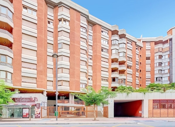 A multi-story residential building with balconies, a covered parking area, and a small commercial space at the ground level.