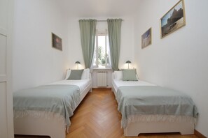 Een kamer met twee eenpersoonsbedden, een raam met gordijnen, twee bedlampjes en een radiator.