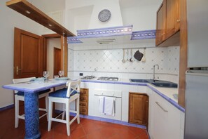 Een kleine keuken met een eettafel, stoelen, een gasfornuis, een spoelbak en houten keukenkastjes.