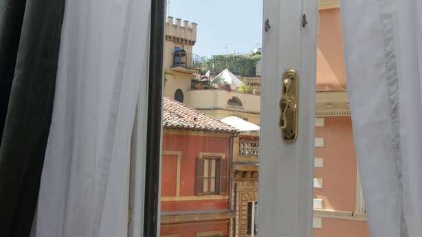 Una vista a través d'una porta oberta amb una finestra, que mostra un edifici amb façanes vermelles i grogues, balcons i un teulat d'uralita.