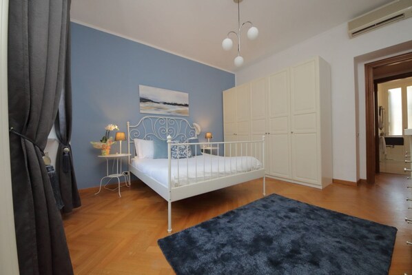 A bedroom with a bed, a white wardrobe, a blue wall, and a painting. - Comodo appartamento con due stanza al Colosseo (Roma)