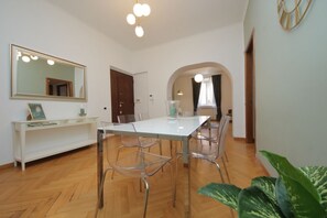 Een eetgedeelte met een witte tafel, transparante stoelen, een spiegel en een plant.