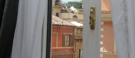 A view through an open door with a window, revealing a building with red and yellow facades, balconies, and a tiled roof.
