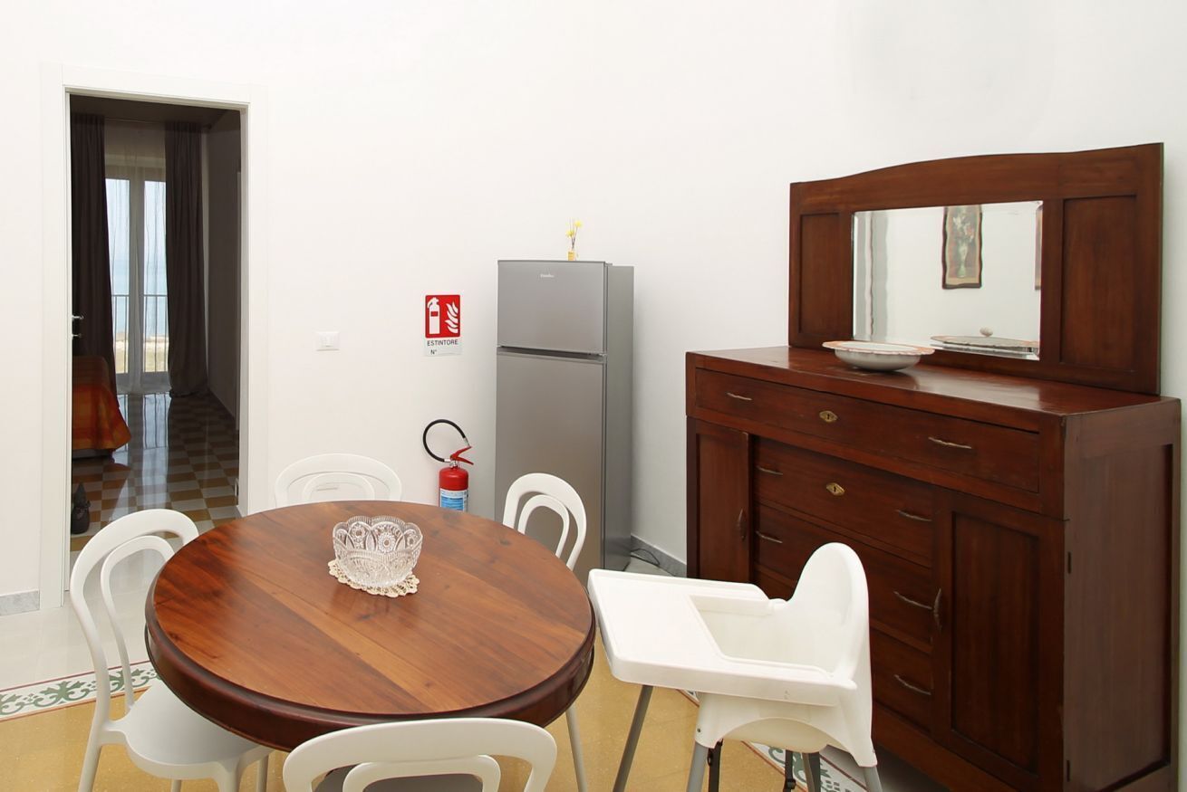 Ein Essbereich mit Holztisch, weißen Stühlen, einem grauen Kühlschrank und einem Holzschrank mit Spiegel.