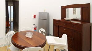 Un comedor con una mesa de madera y sillas blancas, un refrigerador gris y un mueble de madera con espejo.