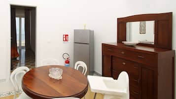 Ein Essbereich mit Holztisch, weißen Stühlen, einem grauen Kühlschrank und einem Holzschrank mit Spiegel.