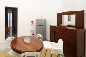 A dining area with a wooden table and white chairs, a gray refrigerator, and a wooden cabinet with a mirror. - Dimora Burrafato, known by locals as “La Casa Rossa”, is a historic summer residence once owned by Princess Pignatelli, located directly on the seafront of Caronia. The property consists of three independent units, each with a private entrance, a bal (Marina di Caronia)