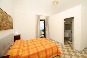 A bedroom with a checkered floor, a bed with a plaid bedspread, a nightstand with a lamp, and a painting on the wall. - Dimora Burrafato, known by locals as “La Casa Rossa”, is a historic summer residence once owned by Princess Pignatelli, located directly on the seafront of Caronia. The property consists of three independent units, each with a private entrance, a bal (Marina di Caronia)