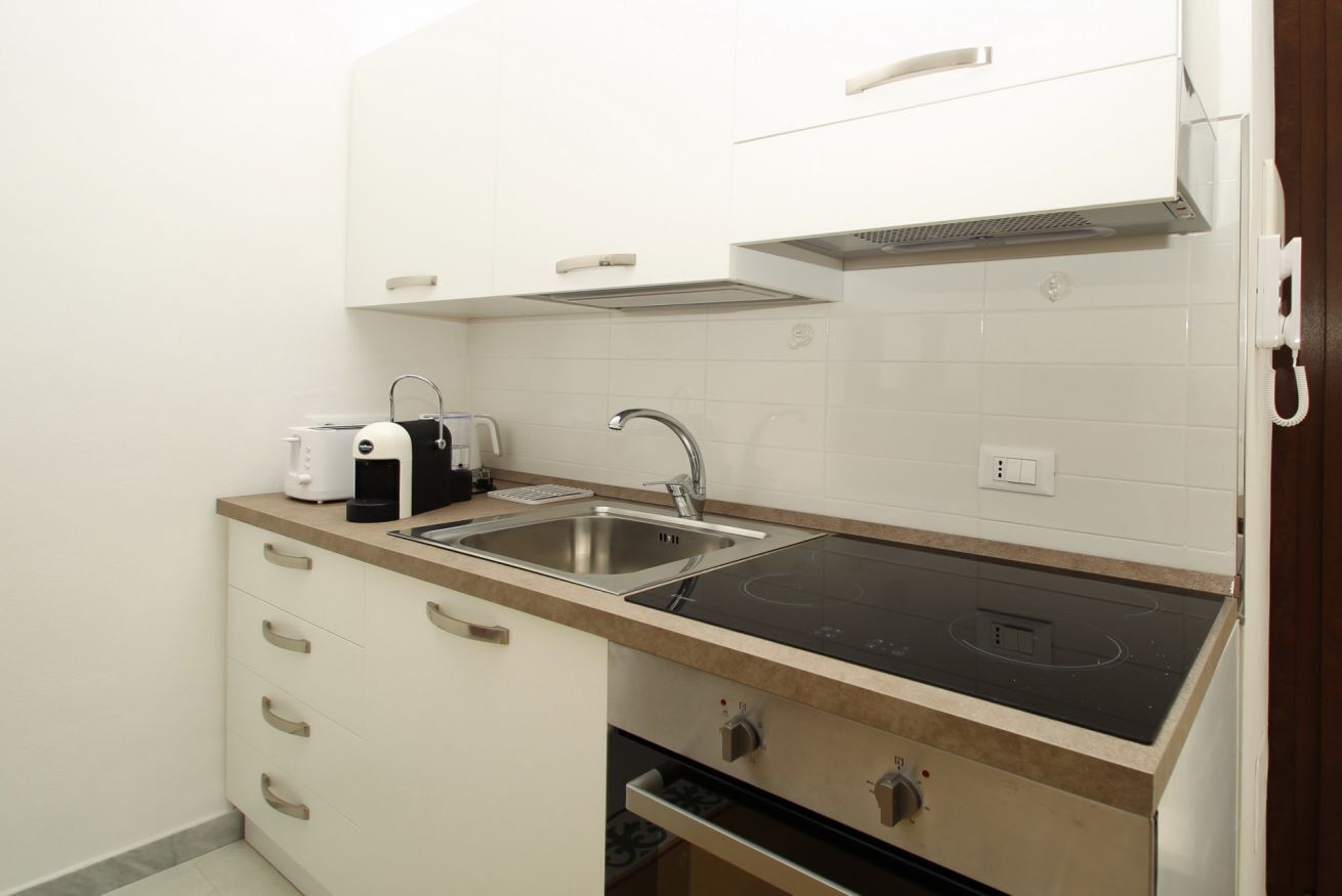 Una cucina compatta con un lavello doppio, piano cottura integrato e mobili bianchi.