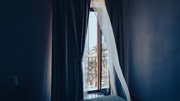 Una stanza con un letto, una finestra con tende leggere e vista su palme.