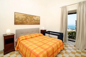 Une chambre avec une couvre-lit à carreaux, une table de chevet avec une lampe, un tableau au mur et un balcon avec des rideaux.