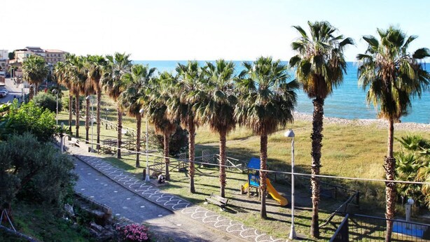 Un paseo marítimo con palmeras, un parque infantil y vistas al mar.
