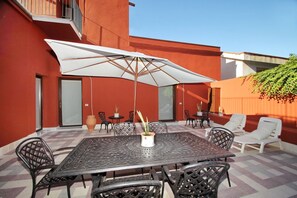 An outdoor patio with a metal table, chairs, a white umbrella, and potted plants. - Dimora Burrafato, known by locals as “La Casa Rossa”, is a historic summer residence once owned by Princess Pignatelli, located directly on the seafront of Caronia. The property consists of three independent units, each with a private entrance, a bal (Marina di Caronia)