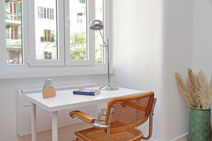 Ein weißer Schreibtisch mit Lampe, Stuhl, Buch und einer Vase mit Trockenpflanzen.