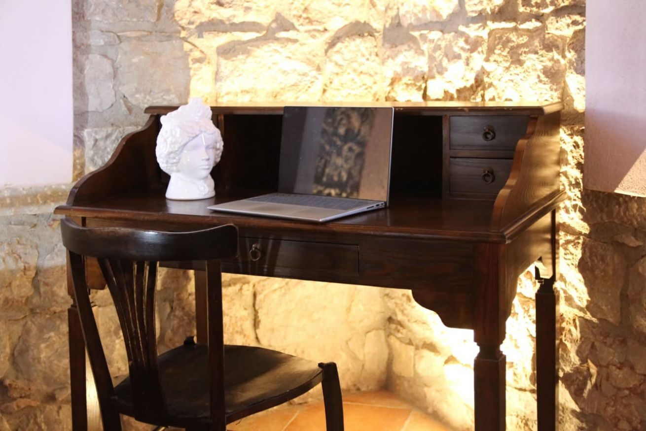 A wooden desk with a laptop, a bust sculpture, and a framed picture.