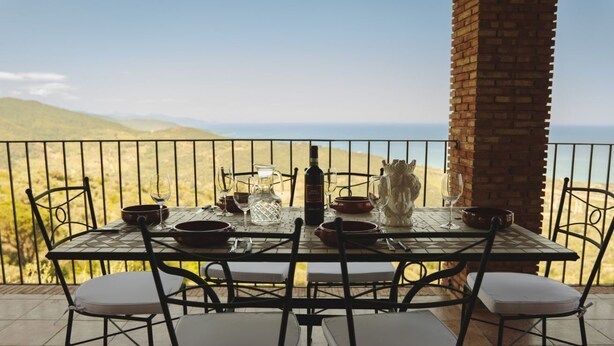 Une table dressée pour quatre personnes, avec vue sur la mer et les collines.
