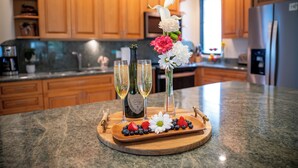 A kitchen counter with a fruit platter, two champagne flutes, and a bottle of wine. - Wailea Elua Village 1702- 2Bdr+2Bath Condominium-Only Steps to the Ocean! (Wailea)