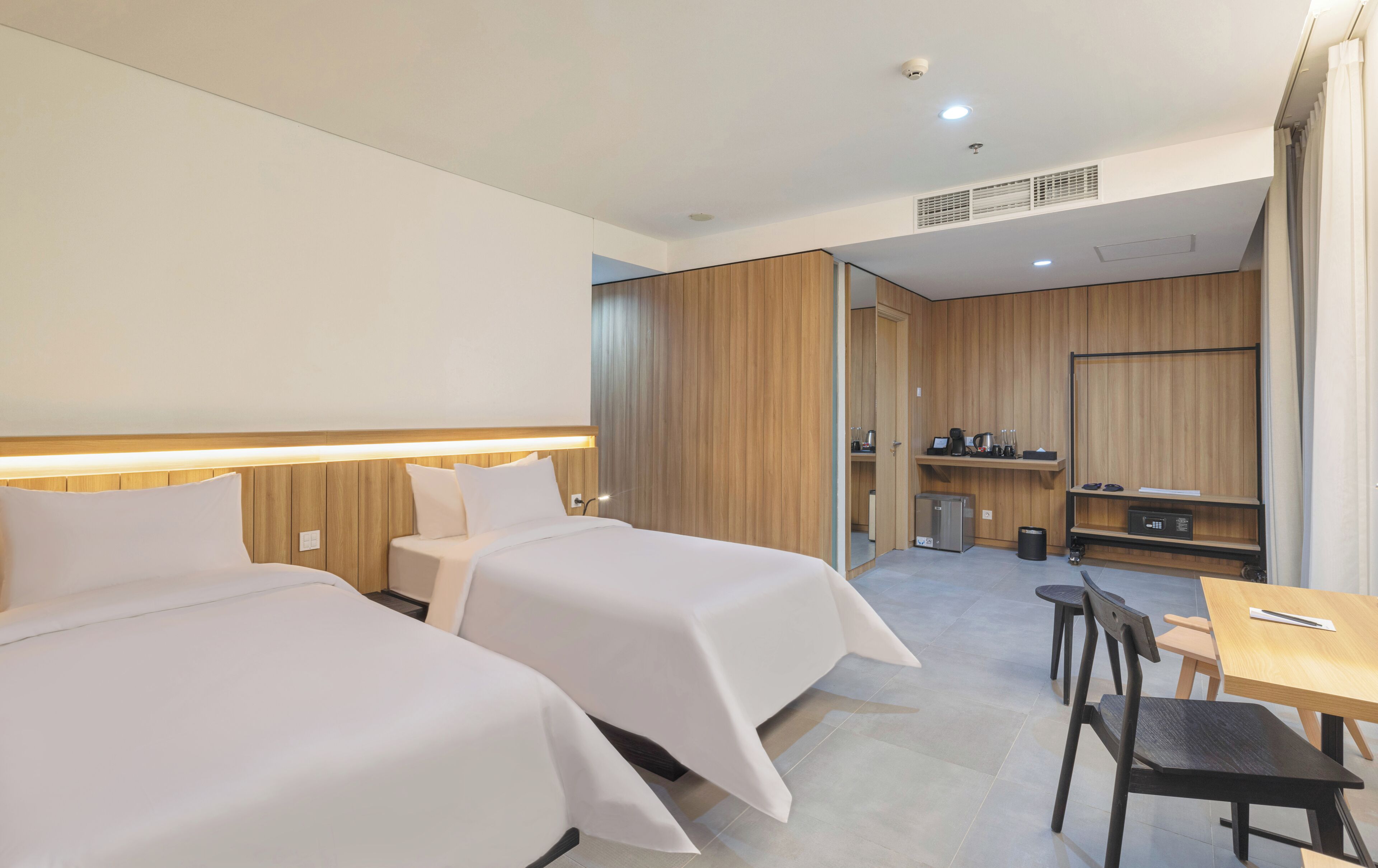 Ein Hotelzimmer mit zwei Betten, einem Schreibtisch, einem Stuhl, einer kleinen Küchenzeile und einem Badezimmer.