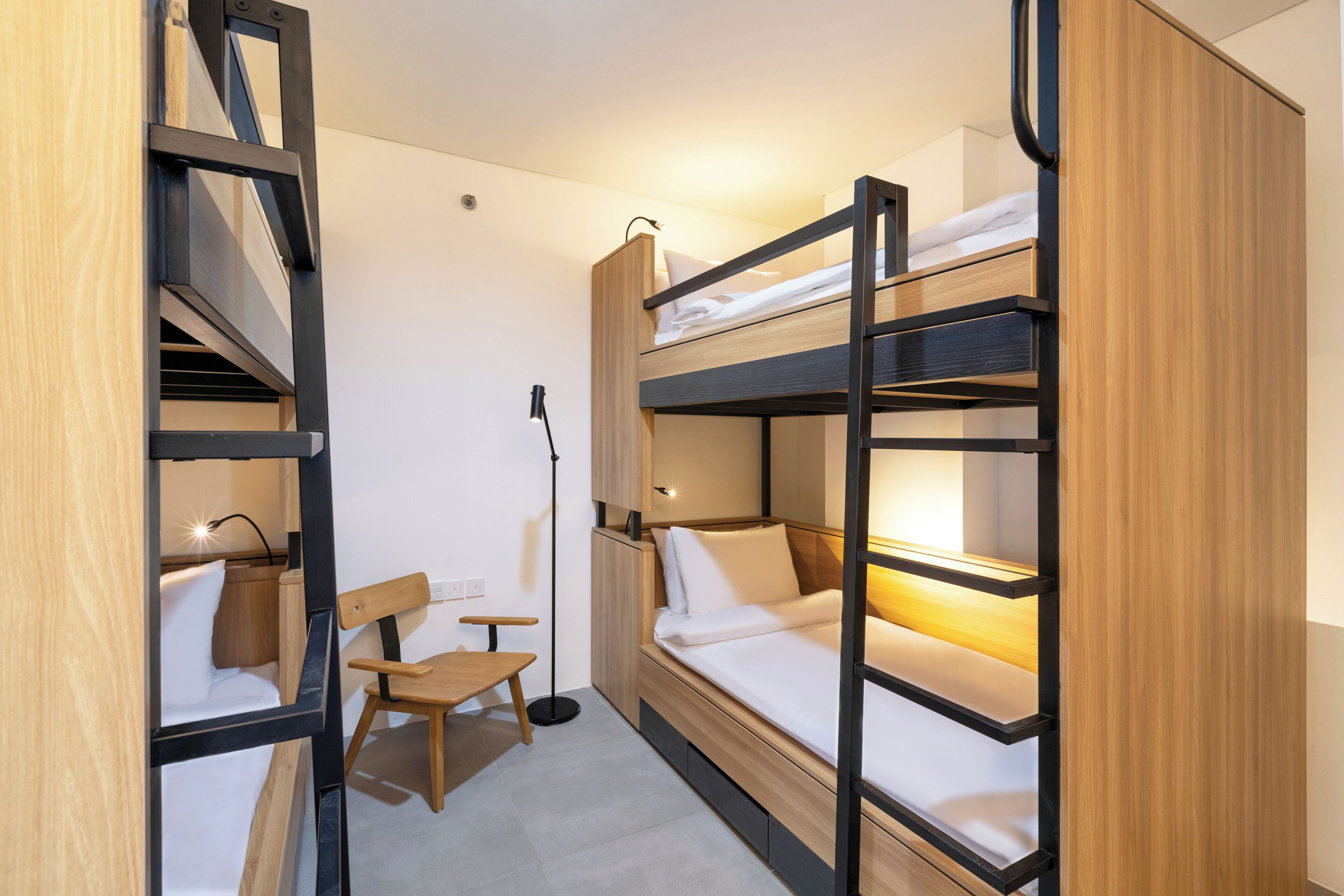 A bunk bed room with a desk and chair, a floor lamp, and a wooden wardrobe.