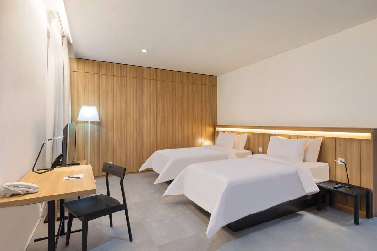 A hotel room with two beds, a desk with a telephone, a chair, a lamp, and a TV.