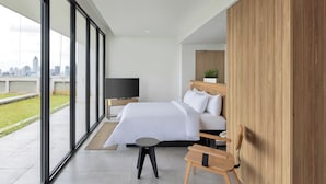 Een moderne hotelkamer met een groot bed, een televisie, een houten hoofdbord en uitzicht op de stad door middel van ramen van de vloer tot aan het plafond.
