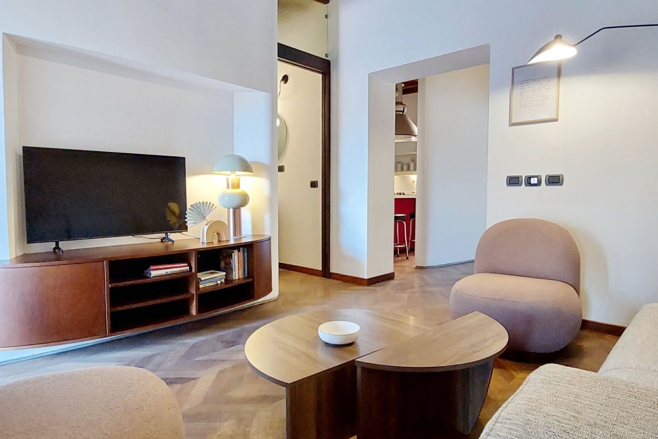 Una sala de estar moderna con una televisión de pantalla plana, un mueble de madera para entretenimiento, una mesa redonda de centro y dos sillones.