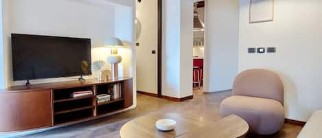 Una sala de estar moderna con una televisión de pantalla plana, un mueble de madera para entretenimiento, una mesa redonda de centro y dos sillones.