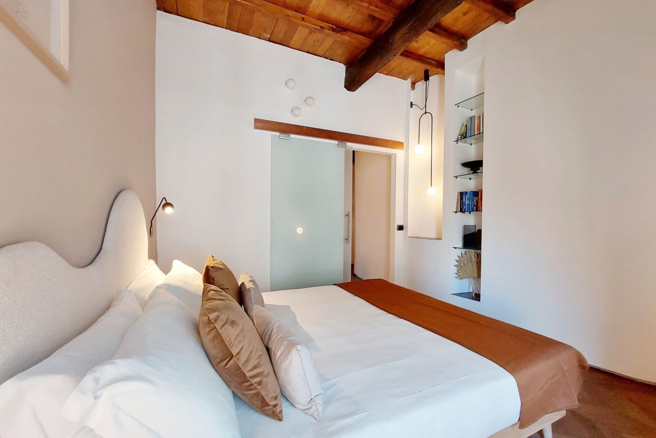 A bedroom with a bed, bedside lamps, a wooden bench, and a bookshelf.