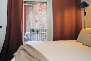 Ein Hotelzimmer mit Bett, einem Balkon mit Tisch und Stühlen sowie Blick auf eine Steinmauer.