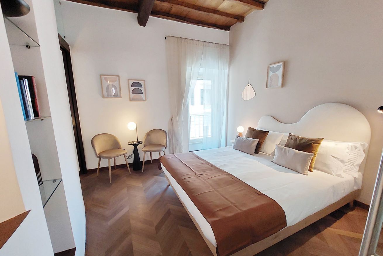 A bedroom with a large bed, two chairs, a small table, and a window with curtains.