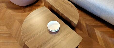 A round wooden coffee table with a bowl on it, placed on a herringbone-patterned floor.