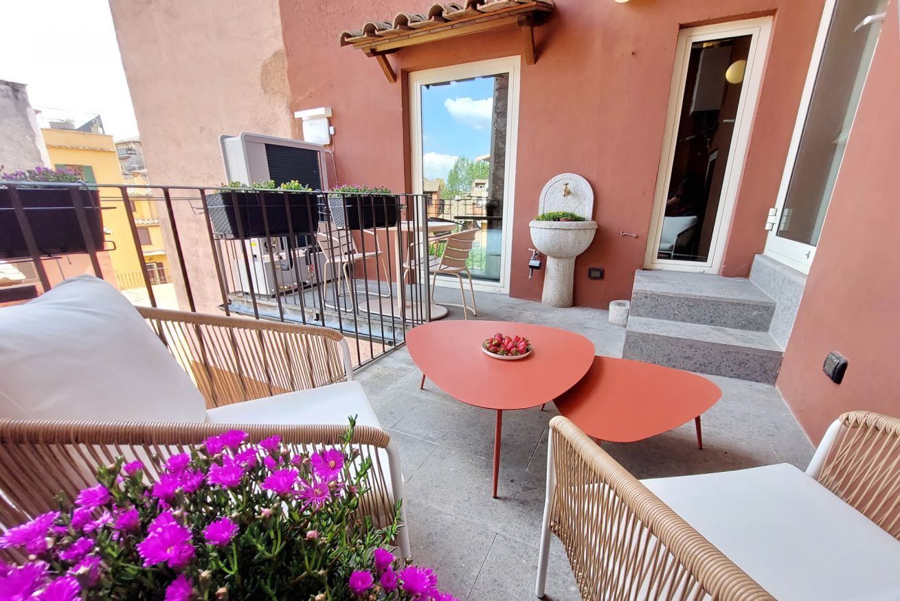 A balcony with wicker furniture, a small table, and a potted plant with pink flowers.