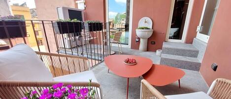 A balcony with wicker furniture, a small table, and a potted plant with pink flowers.