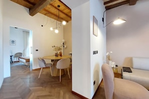 Een moderne woonkamer met een bank, een eettafel met stoelen en een keukenhoek met een koelkast en een bijzettafeltje met decoratieve objecten.