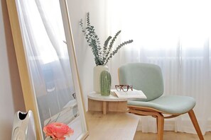 Ein Zimmer mit einem hellgrünen Stuhl, einem Kaktus und einer Vase mit Grünpflanzen.