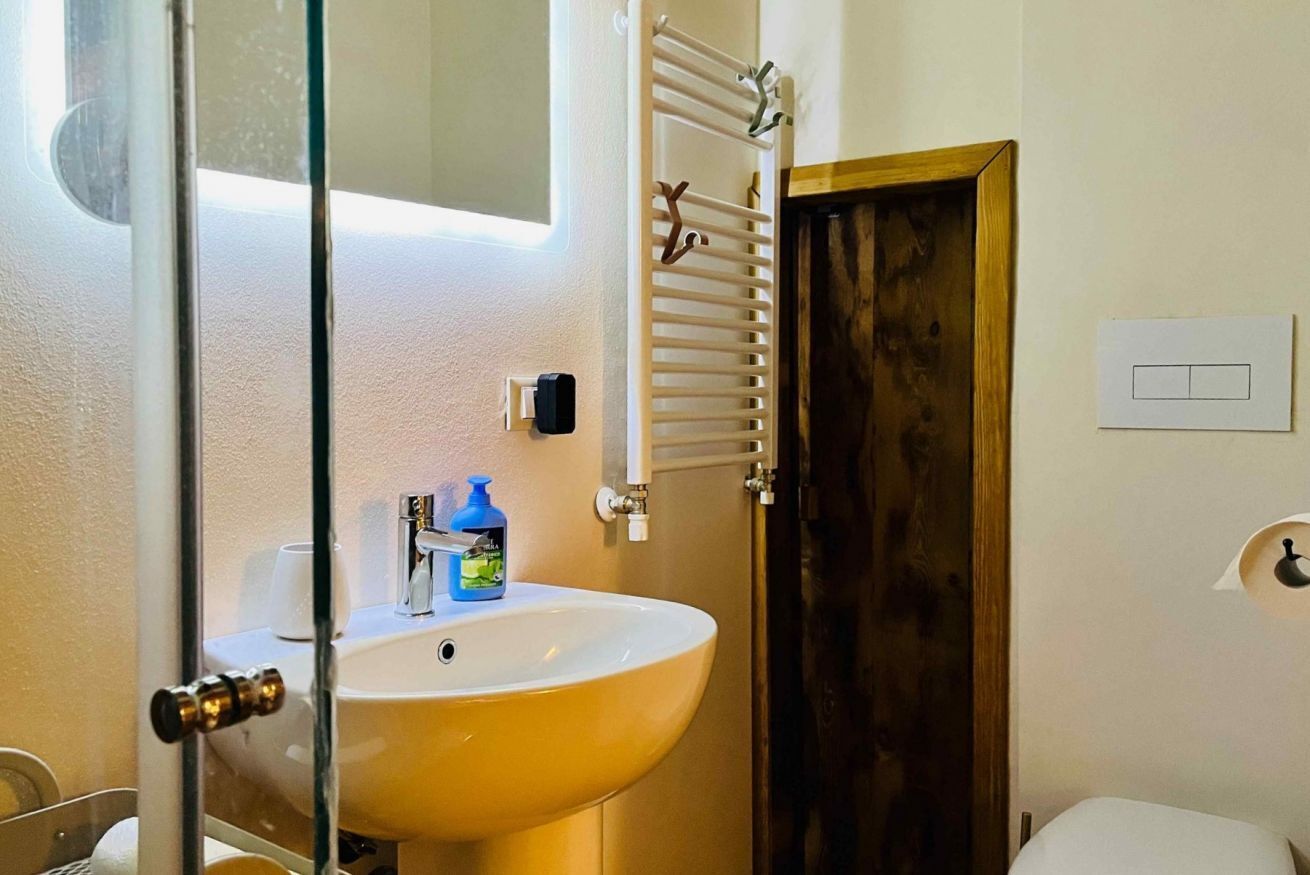Ein Badezimmer mit einem gelben Waschbecken, einer Duschkabine aus Glas, einem weißen Handtuchhalter und einer Holztür.