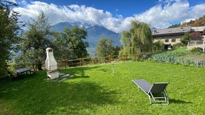 A grassy outdoor area with a stone structure, a metal bench, and a wooden fence. - GuestHost - Charming 70 sqm apartment on two levels, comfortably accommodating four people.The property is located in La Salle, in the hamlet of Cottin, surrounded by Alpine nature at the foot of Mont Blanc, an ideal location for skiers and outdoor sport (La Salle)