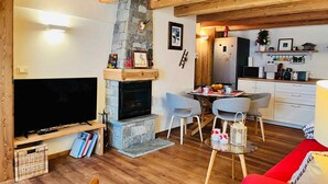 A living room with a fireplace, a television, and a dining area with chairs and a table. - GuestHost - Charming 70 sqm apartment on two levels, comfortably accommodating four people.The property is located in La Salle, in the hamlet of Cottin, surrounded by Alpine nature at the foot of Mont Blanc, an ideal location for skiers and outdoor sport (La Salle)