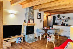 Een woonkamer met een open haard, een televisie en een eethoek met stoelen en een tafel.