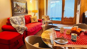 A cozy room with a red sofa, a dining table with a red tablecloth, and a painting on the wall. - GuestHost - Charming 70 sqm apartment on two levels, comfortably accommodating four people.The property is located in La Salle, in the hamlet of Cottin, surrounded by Alpine nature at the foot of Mont Blanc, an ideal location for skiers and outdoor sport (La Salle)